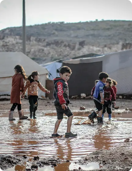 Children walking through muddy ground near tents